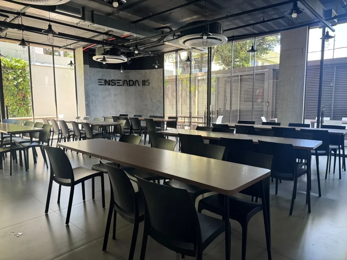 Refeitório do Enseada 115 com mesas coletivas e fachada envidraçada